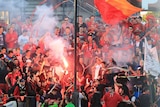 Soccer fans stand around a flare in the grandstands.