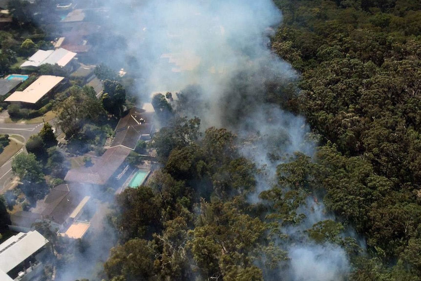 An aerial photo of a bushfire burning close to the backyards of several Castle Cove homes.