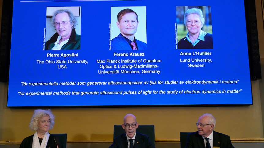 Two men and a woman are seated at a desk below a blue slide showing the faces and biographies of two other men and a woman.