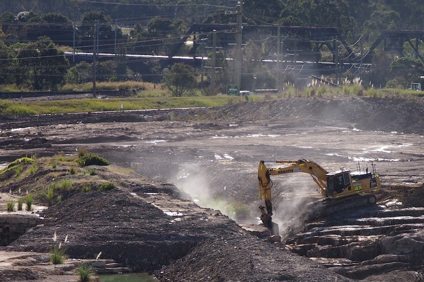 Tractor digging material from the centre of the smelter site with Main rd in background