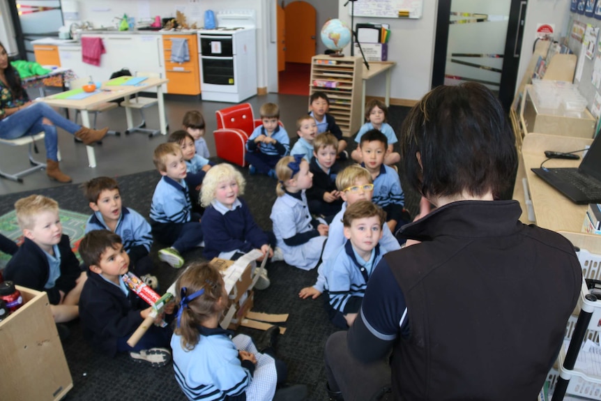 A teacher sits in front of a class of kindergarten students.