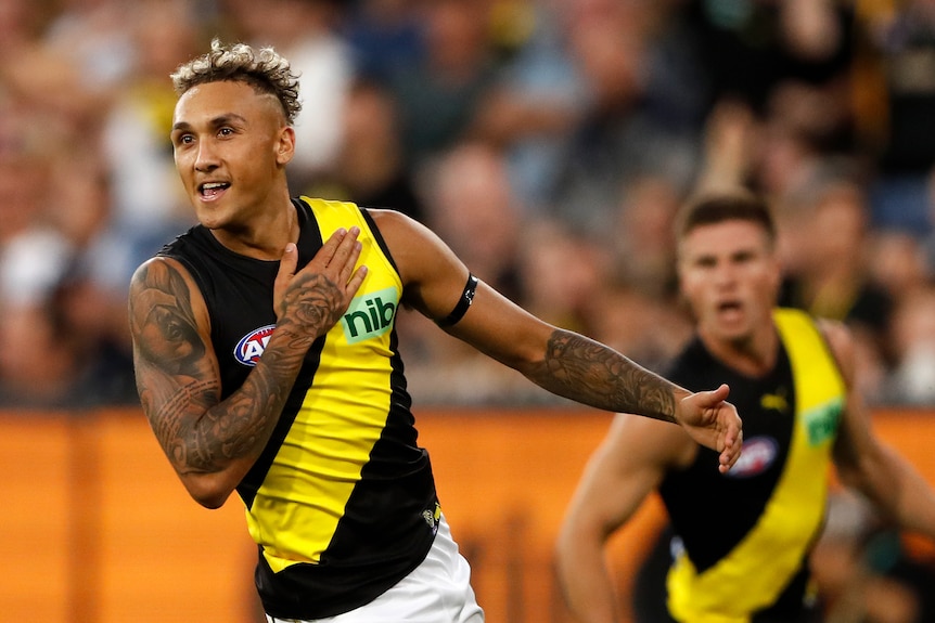 A Richmond AFL player smiles and thumps his chest with his hand after kicking a goal.