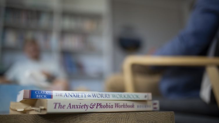 Blurred image of two men talking with books about anxiety in the foreground