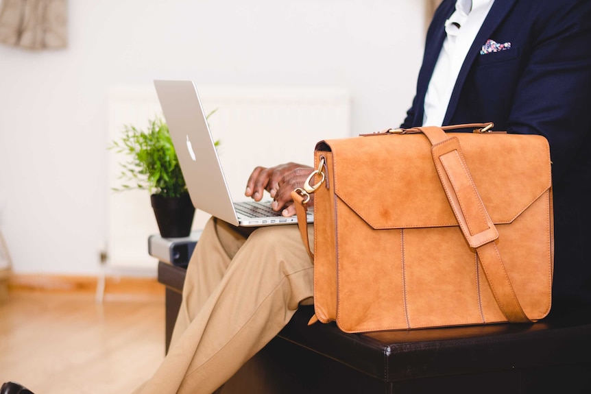 A man in khaki trousers and a navy blazer looks at a computer to depict a business appropriate wardrobe for men.