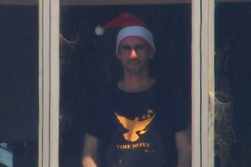 Mostafa Azimitabar who is in refugee detention, stands at the window of the hotel where lives wearing a santa hat.