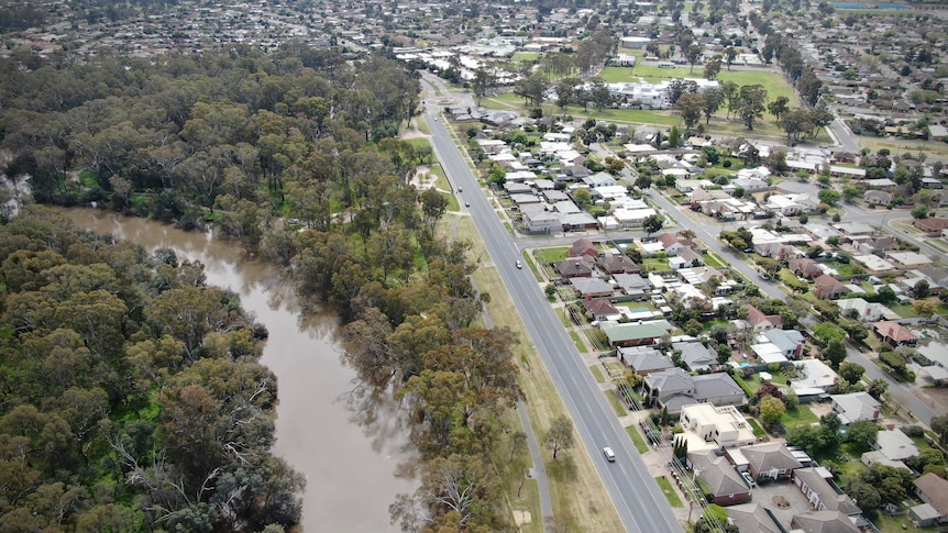 Shot from the air, a tree-lined river on the left sits beside suburban homes on the right
