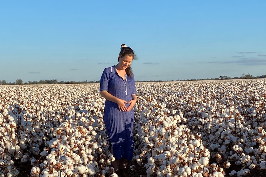 woman cradling baby bump in blue dress in cotton field