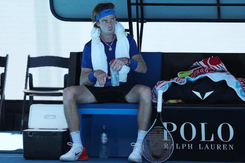 A Russian male tennis player sits at a change of ends at Australian Open.