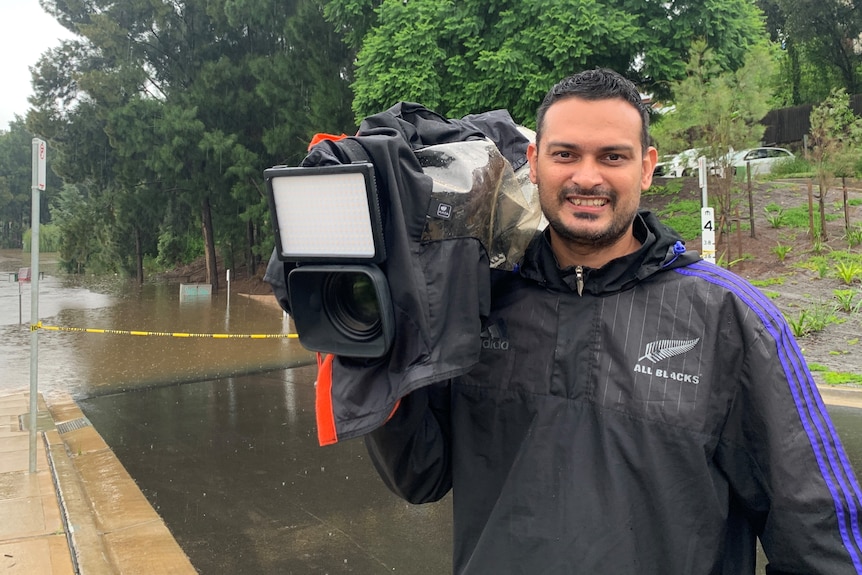 Man holding camera with water across road behind him.