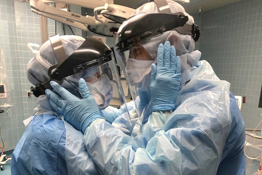 A man and a woman in full protective gear clutch each others faces