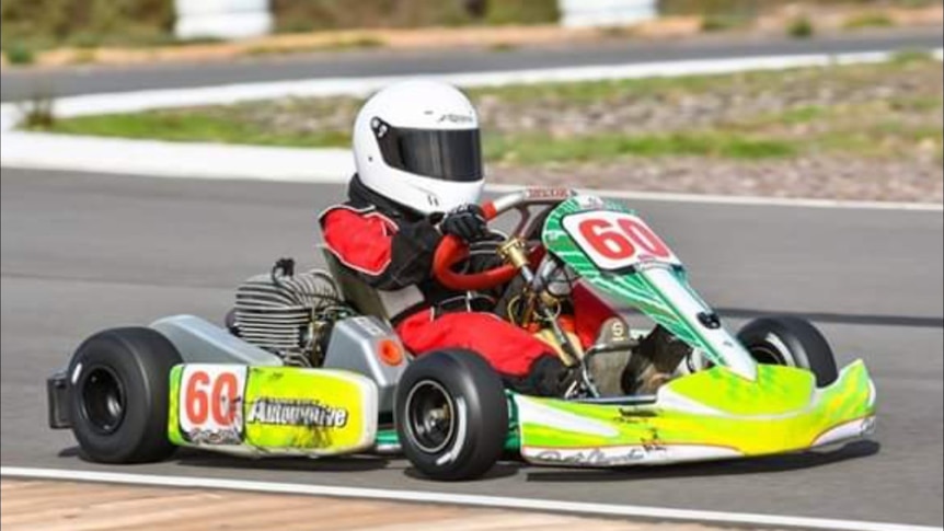 boy in white helmet and red and black racing suit in a florescent yellow go-kart.