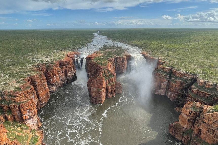 A wide scenic aerial shot of 100 metre high waterfalls with water gushing over the cliffs.