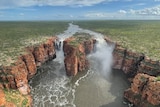 A wide scenic aerial shot of 100 metre high waterfalls with water gushing over the cliffs.