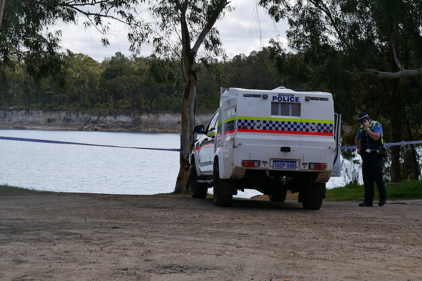A police vehicle and officer in front of police tape at the side of a lake