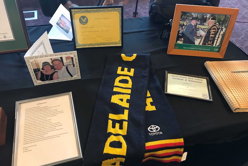 A table with a scarf, framed certificates and pictures and cards on it