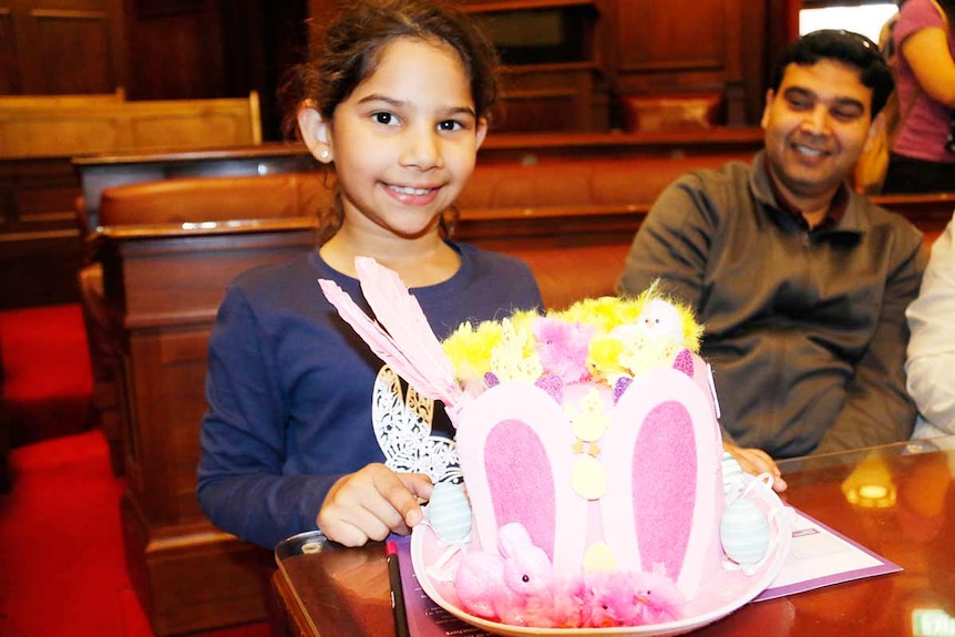 A girl holds brightly coloured pink Easter hat.