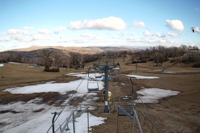 patches of snow on grass with ski lifts overhead