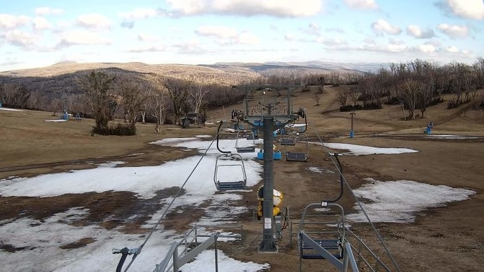 patches of snow on grass with ski lifts overhead