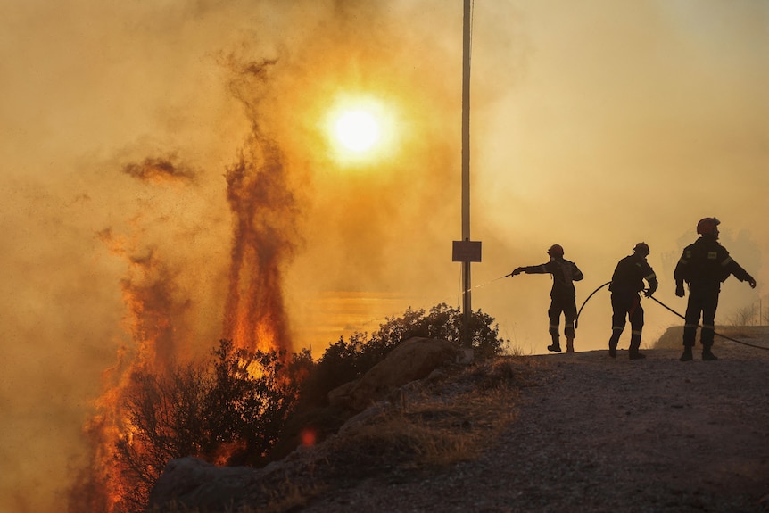 A silhouette of firefighters putting out a blaze with the sun in the background.