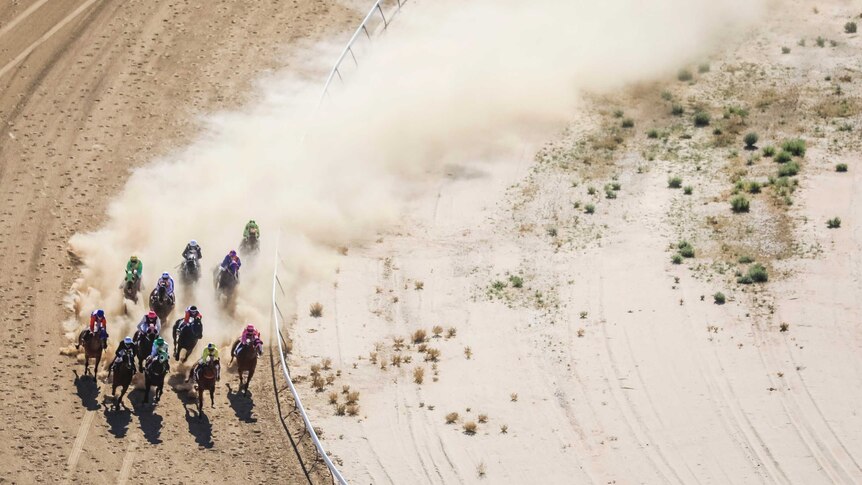 An aerial view of jockeys in colourful jerseys racing horses around the dirt racecourse at the Birdsville races.