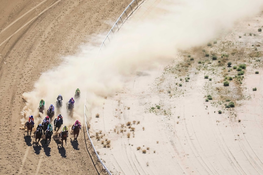 An aerial view of jockeys in colourful jerseys racing horses around the dirt racecourse at the Birdsville races.