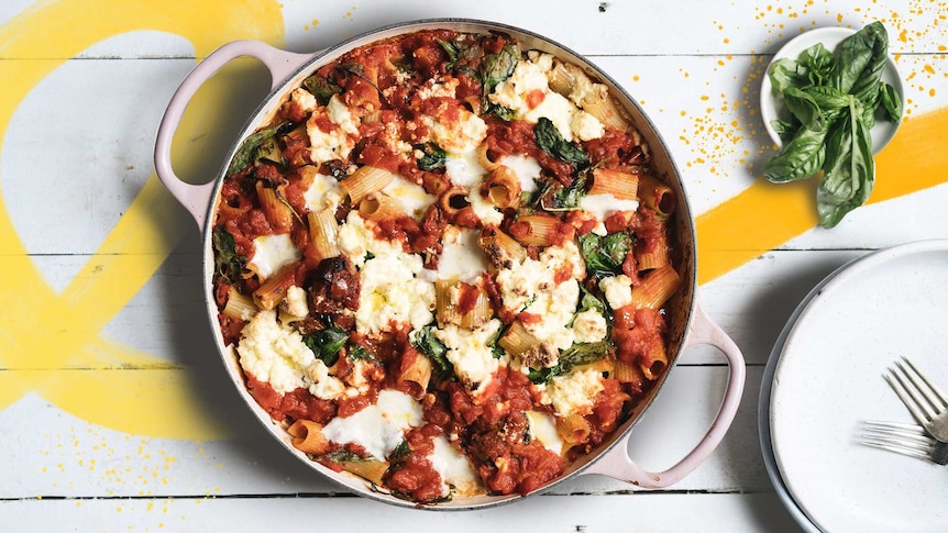 A pan filled with baked tomato pasta topped with cheese and spinach to depict recipes using pantry staples like pasta and beans.