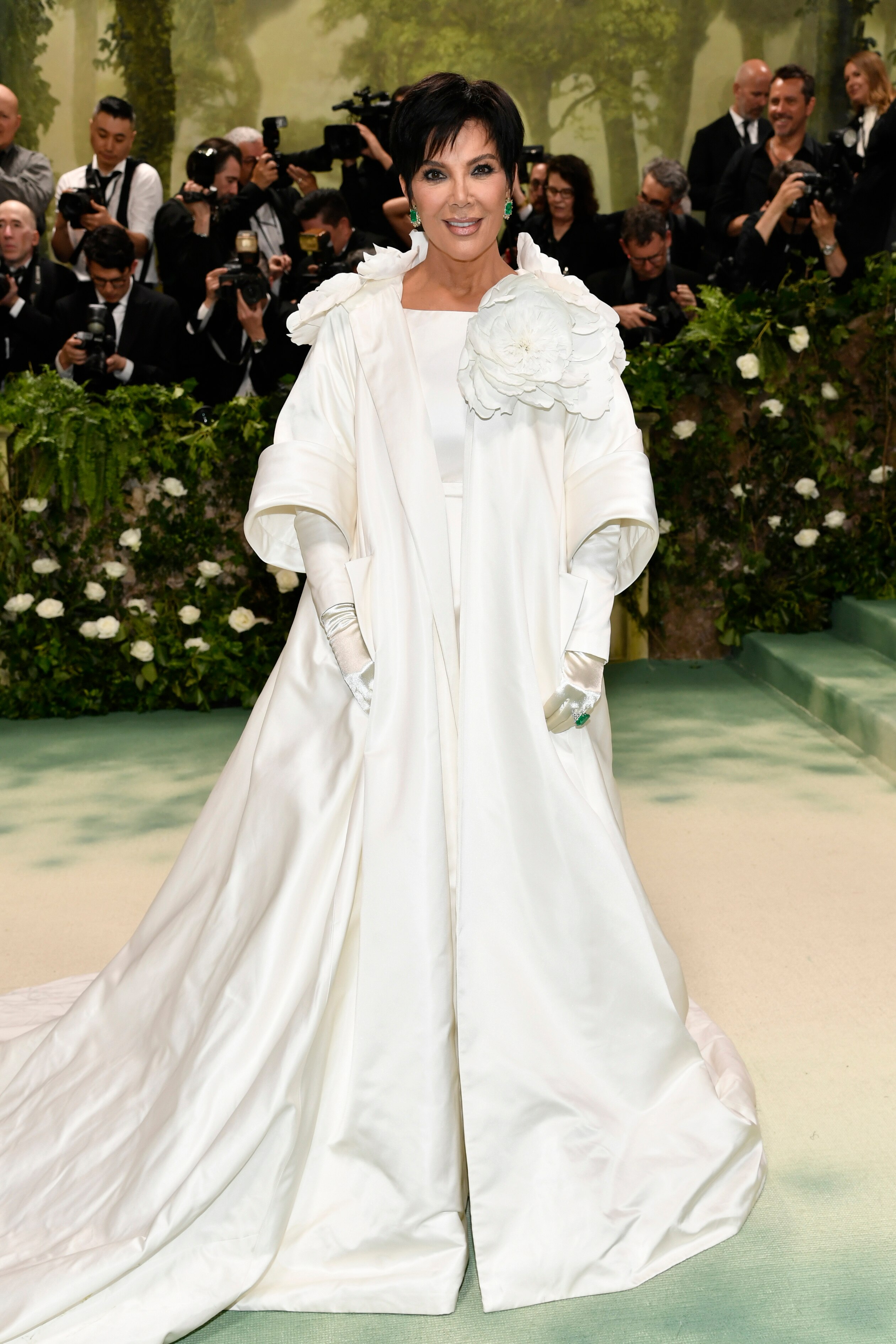 Kris Jenner wearing a long white coat with flowers on the shoulders and long white gloves