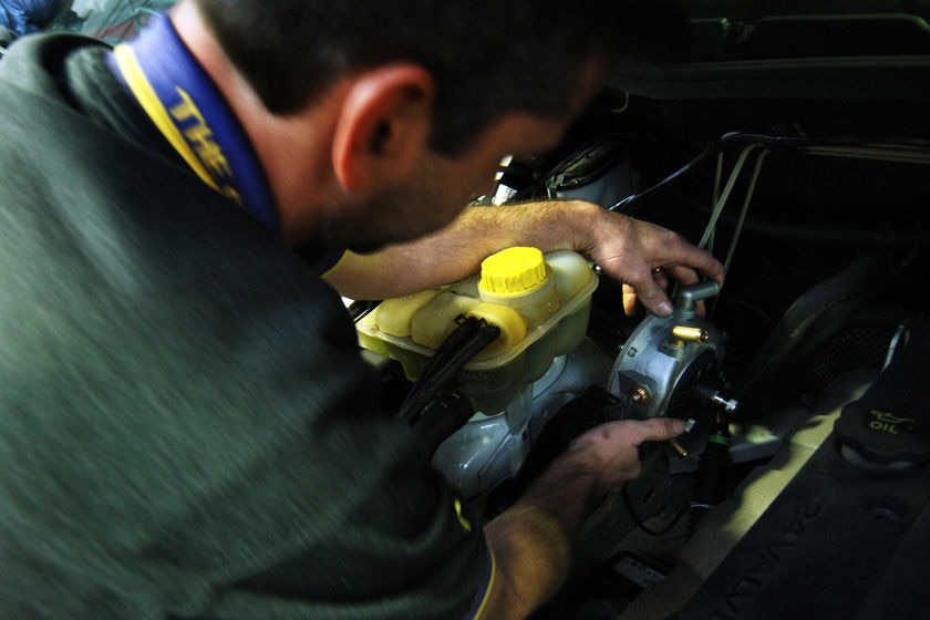 A close-up on a man with black hair working on a car engine.