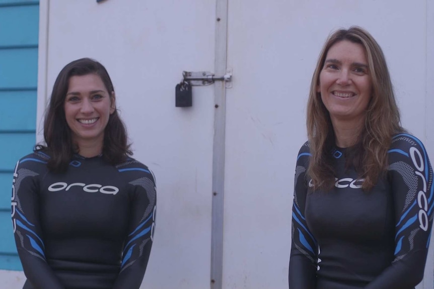 Two women in wetsuits smile for a portrait
