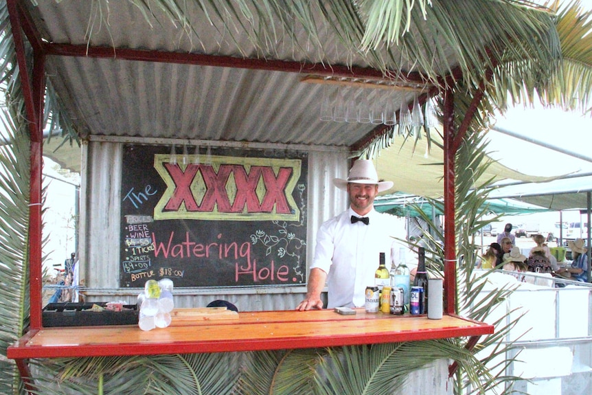 Joshua Borowski standing at the bar at Come by Chance Picnic Races, a tin shed decorated with palm leaves.