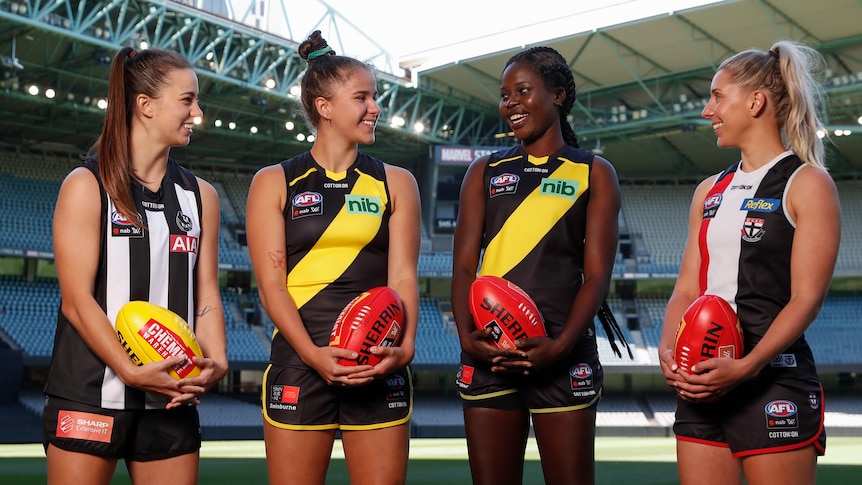 Chloe Molloy, Ellie McKenzie, Akec Makur Chuot and Hannah Priest smile while holding footballs at Marvel Stadium