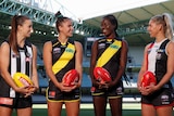 Chloe Molloy, Ellie McKenzie, Akec Makur Chuot and Hannah Priest smile while holding footballs at Marvel Stadium