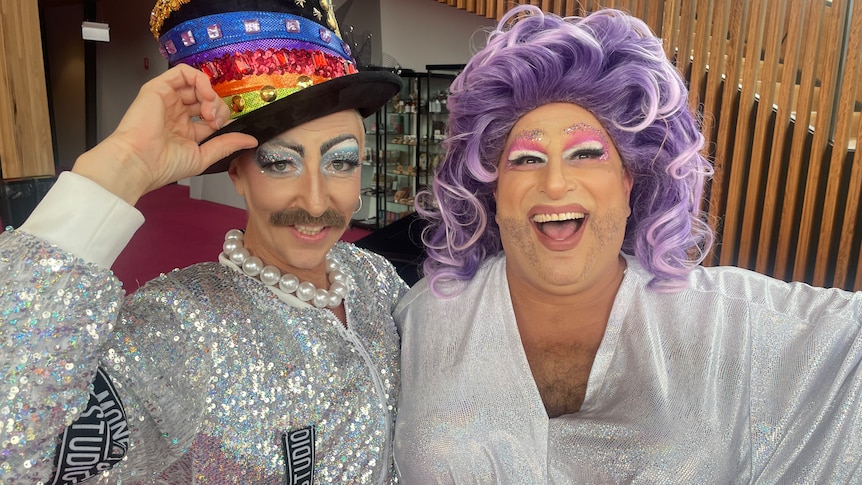 Two drag performers, one in a top-hat with moustache and another in a purple wig