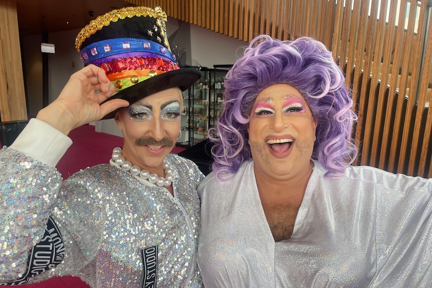 Two drag performers, one in a top-hat with moustache and another in a purple wig