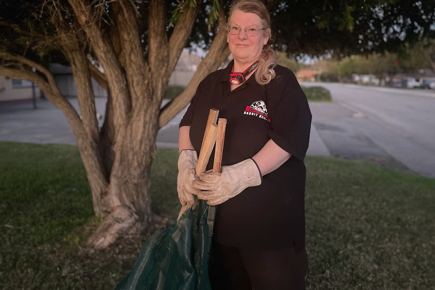 A woman in gardening gloves holds a net at dusk