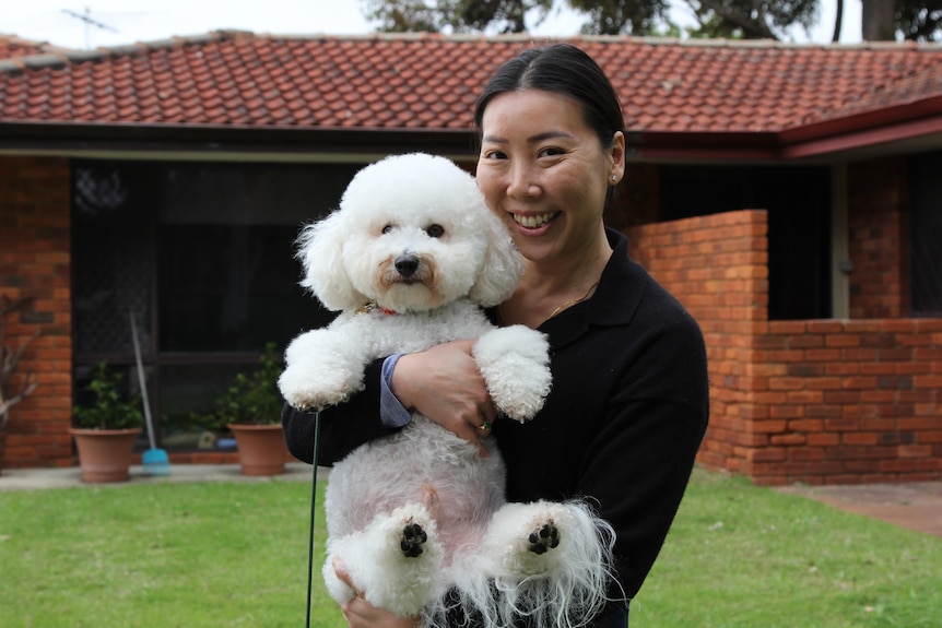 Ada Chung smiling and holding her fluffy white dog Genghis outside.