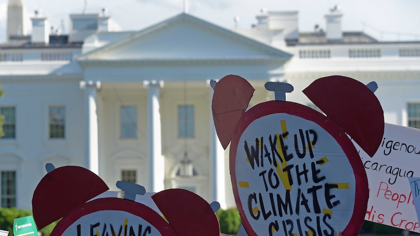 Protest signs demanding climate change action are held up in front of the White House