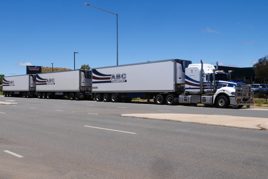 A road train towing three trailers parked on the side of the road.