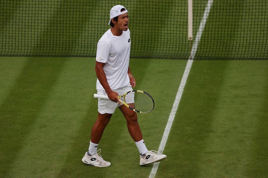 Wearing his cap backwards, an Australian men's tennis player roars in celebration after winning a big point at Wimbledon.
