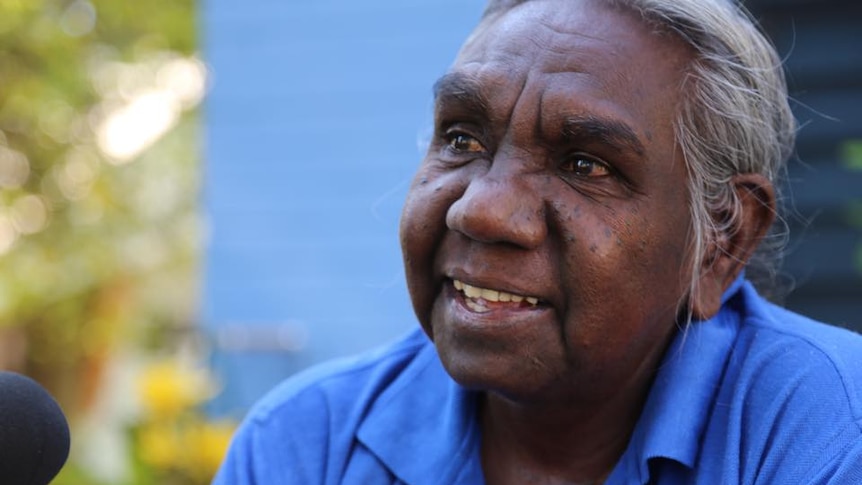 An elderly Indigenous woman speaks into a microphone.