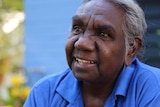 An elderly Indigenous woman speaks into a microphone.