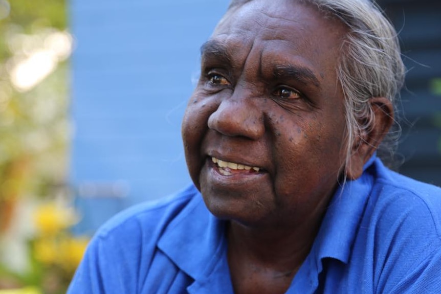 An elderly Indigenous woman speaks into a microphone.