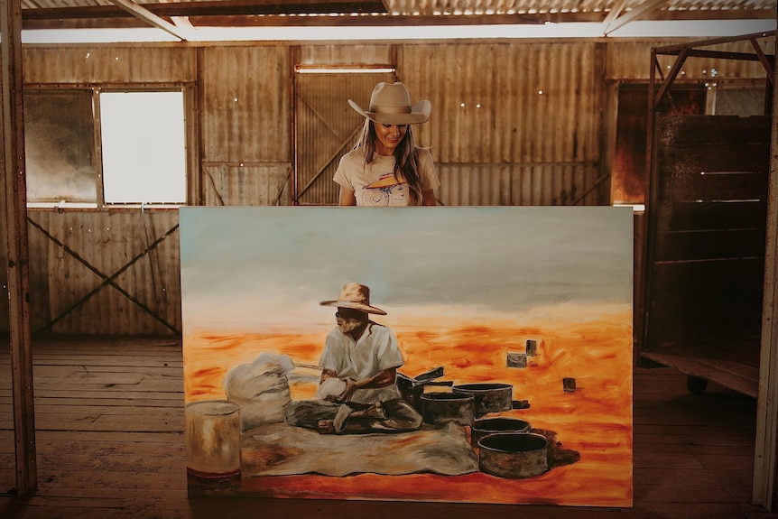 Woman standing with large canvas showing man cooking at campfire