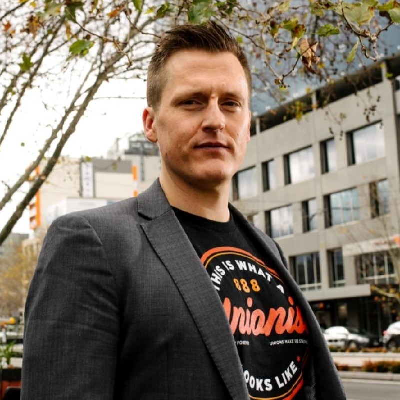 A man wearing a suit jacket over a black T-shirt with writing on it