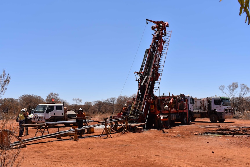 A drill rig in action on a mine set taking samples being operated by two men dressed in orange