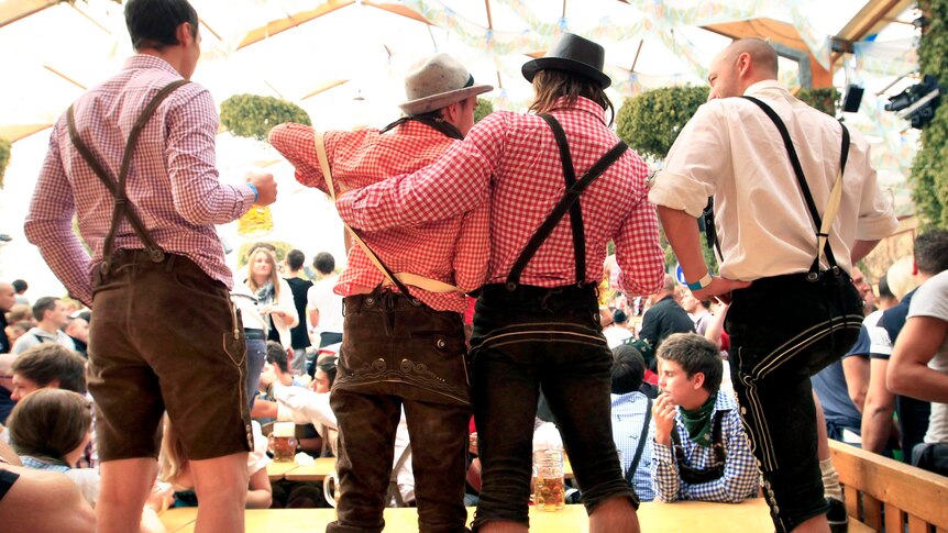 Revellers in traditional Bavarian leather trousers toast with beer during Oktoberfest.