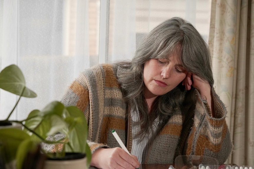 A white woman with greying brown hair writing something on a table