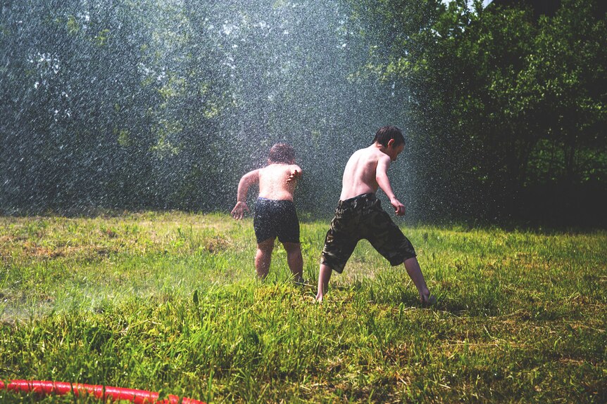 Two children playing with a sprinkler
