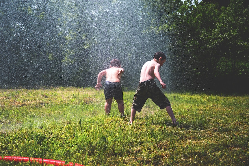 Two children playing with a sprinkler