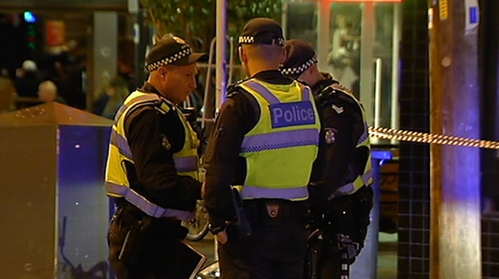 Three police officers speak to each other in front of a scene marked by police tape.
